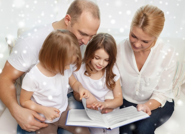 rodzina, wypoczynek, edukacja i ludzie - uśmiechnięta matka, ojciec i małe dziewczynki czytające książkę na tle płatków śniegu