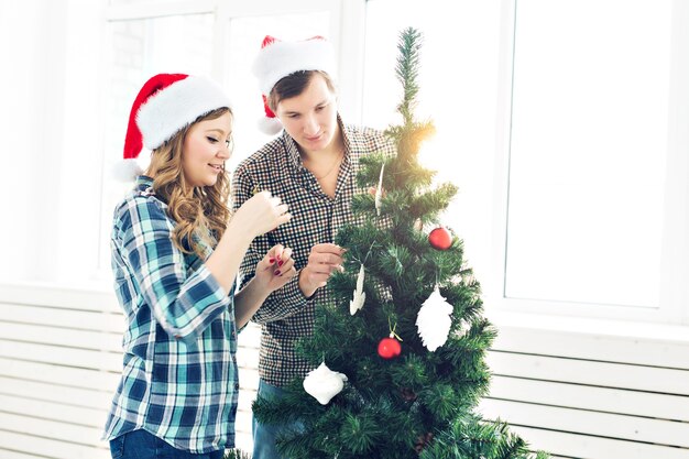 Rodzina, x-mas, ferie zimowe i koncepcja ludzie - szczęśliwa młoda para dekorowanie choinki w domu.