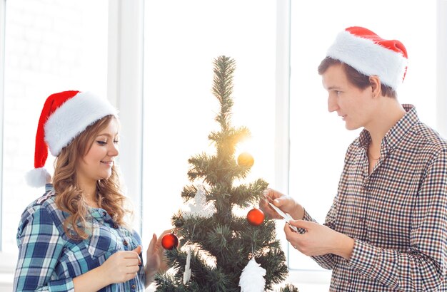 Rodzina, x-mas, ferie zimowe i koncepcja ludzie - szczęśliwa młoda para dekorowanie choinki w domu.