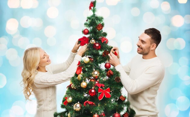 rodzina, x-mas, ferie zimowe i ludzie koncepcja - szczęśliwa para dekorowanie choinki na niebieskim tle świateł świątecznych