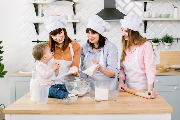 Rodzina Z Babcią, Dwiema Córkami I Małą Dziewczynką Do Pieczenia W Kuchni. Babka Dodaje Cukier Do Ciasta. Koncepcja Dnia Matki, Rodzinne Wypieki