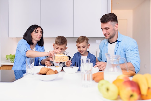 Rodzina Z Dwoma Synami Jedzącymi Zdrowe Poranne śniadanie Z Płatkami Kukurydzianymi I Mlekiem