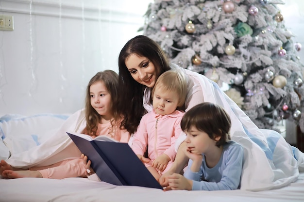 Rodzina z dziećmi bawiąca się na łóżku pod kołdrą podczas Świąt Bożego Narodzenia