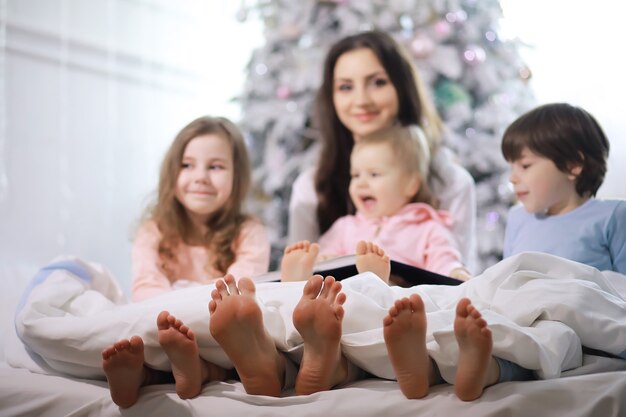 Rodzina z dziećmi bawiącymi się na łóżku pod kołdrą podczas świąt Bożego Narodzenia.