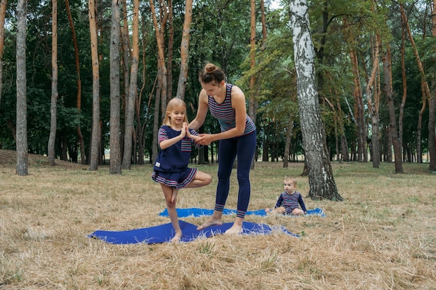 Rodzinna fitness i joga szczęśliwa mama ćwicząca z dziewczynkami na trawiastej ziemi na tle drzew w lesie