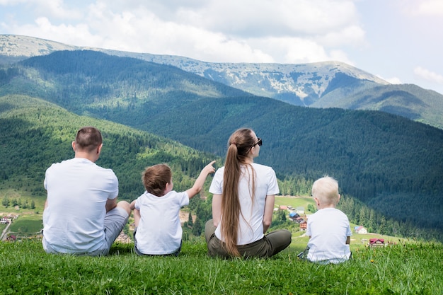 Rodzinne wakacje. Rodzice i dwaj synowie podziwiają widoki na góry. Widok z tyłu. Słoneczny letni dzień