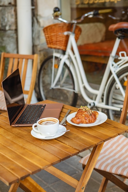 Rogalik z laptopem i kawa na letnim tarasie kawiarni