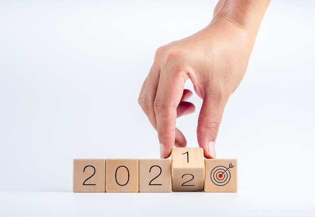 Rok kalendarzowy 2021 zmienił się na 2022 z celem i udaną koncepcją. Ręcznie obracając drewniane klocki kostki do przejścia od 2021 do 2022 ze znakiem ikony celu na białym tle.