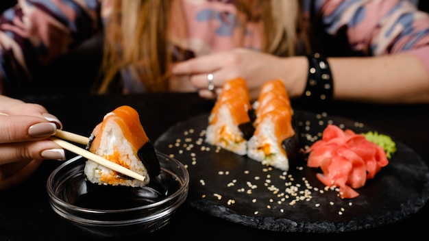 Zdjęcie roladki sushi z imbirem i wasabi. tradycyjna kuchnia orientalna. zdrowe odżywianie. kobieta trzymająca bułkę z pałeczkami