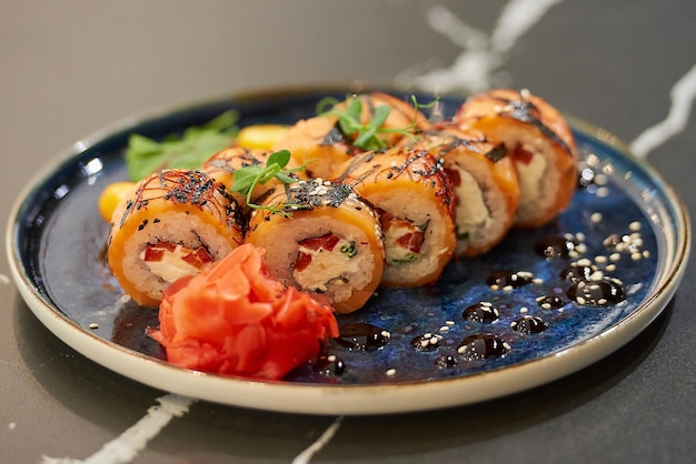 Roladki sushi z łososiem z serkiem Philadelphia i tuńczykiem na niebieskim talerzu ceramicznym z sosem sezamowym wasabi i liśćmi Stół z czarnego kamienia