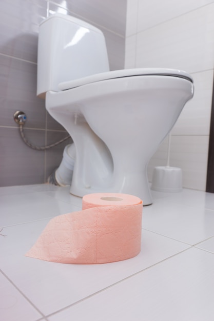 Rolka Miękkiego Różowego Papieru Toaletowego W łazience Stojącej Na Białej Podłodze Wyłożonej Kafelkami W Pobliżu Zwykłego Białego Toalety Lub Toalety, Niski Kąt Widzenia