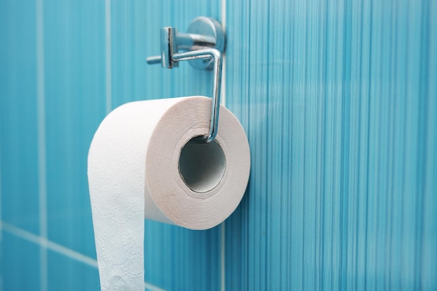 Rolka papieru toaletowego wisi na metalowym uchwycie na ścianie z niebieskich płytek