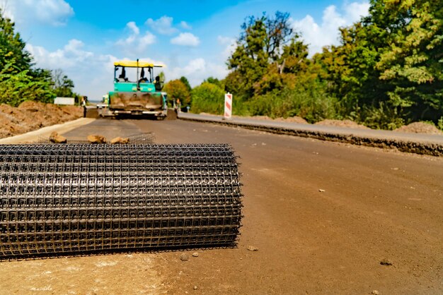 Rolka siatki zbrojonej układa się na drodze na tle profesjonalnego sprzętu do naprawy dróg Zbliżenie