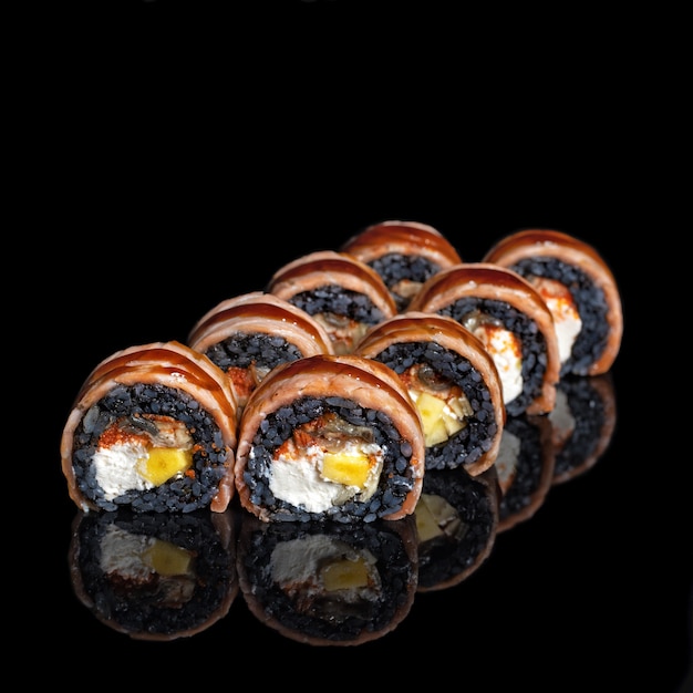 Rolka sushi Golden Dragon. Sushi Rolls z czarnym ryżem, łososiem, mango z odbiciem na czarnym tle. Ścieśniać. Kuchnia japońska. Zdjęcie do menu