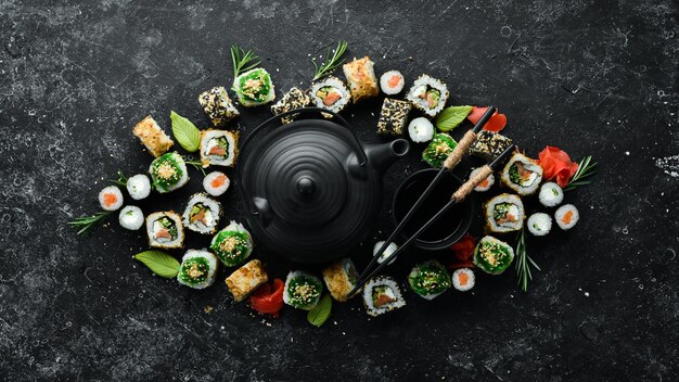 Rolki sushi i czajniczek z herbatą na czarnym tle kamienia Świetny zestaw japońskich potraw