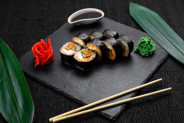 Rolki sushi ułożone na ciemnym tle ozdobione liśćmi bambusa i pałeczkami