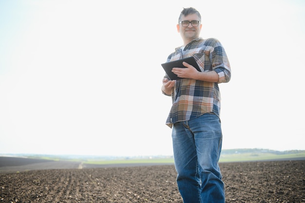 Rolnik pracuje na polu wiosną z tabletem Starszy rolnik patrzy na tabletkę i zielone pędy Sprytny agronom z tabletem w dłoniach sprawdza pole Rolnictwo przyjazne dla środowiska