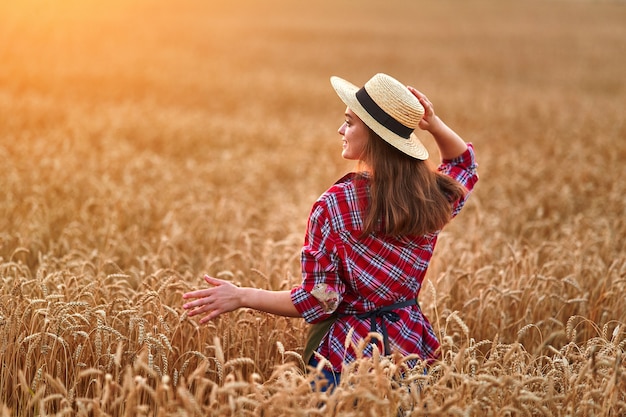 Rolnik stojący samotnie podczas spaceru przez żółte pole suchej dojrzałej pszenicy wśród złotych kłosków o zachodzie słońca