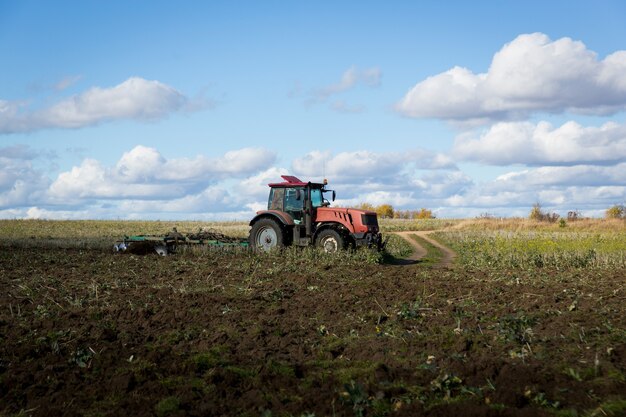 Rolnik traktorem, maszynami rolniczymi, uzdatnia ziemię kultywatorem. Nowoczesny czerwony traktor w polu. Orka ciężkim ciągnikiem podczas uprawiania prac rolniczych na polu pługiem.