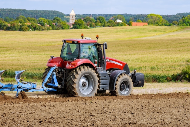 Rolnik W Czerwonym Ciągniku Przygotowujący Ziemię Pługiem Do Siewu