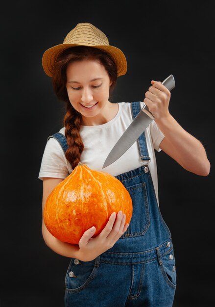 Rolnik w kombinezonie na czarnym tle wycina z dyni lampion nożem na halloween