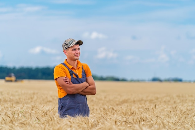 Rolnik w pomarańczowym i niebieskim mundurze stojący na dużym pięknym żółtym polu ze skrzyżowanymi rękami i odwracającym wzrok Zapierający dech w piersiach widok na horyzont i niebo