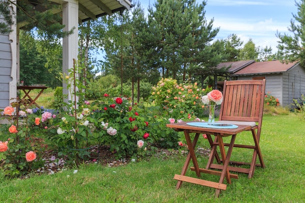 Romantyczna część wypoczynkowa w ogrodzie różanym okrągły drewniany stół i krzesła w pobliżu dużych kwitnących krzewów angielskich róż