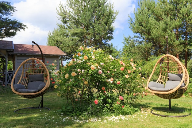 Romantyczna część wypoczynkowa w ogrodzie różanym, okrągły drewniany stół i krzesła w pobliżu dużych kwitnących krzewów róż