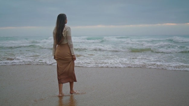Romantyczna dziewczyna z widokiem na ocean wieczorem marząca kobieta spacerująca po burzliwej plaży