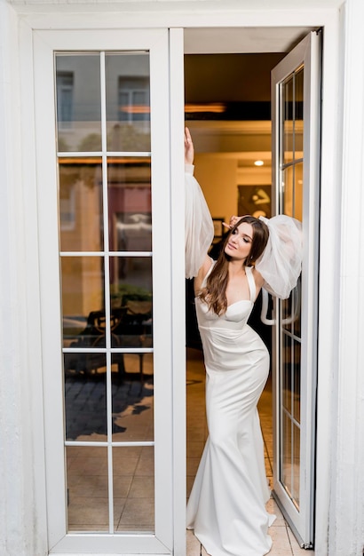 Romantyczna i piękna kobieta w białej sukni ślubnej w pobliżu pięknej willi przy białym oknie