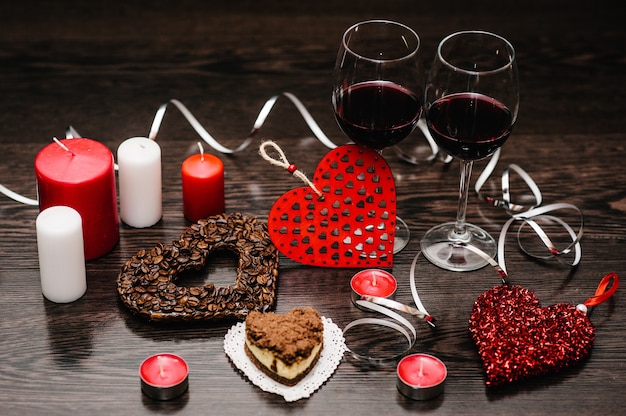 Zdjęcie romantyczna kolacja, świeczki, koncepcja walentynek. ciasto, kieliszki wina. serce z ziaren kawy. zdobione czerwone serca na brązowej powierzchni drewnianej. kompozycja miłości. miejsce na tekst. widok z boku