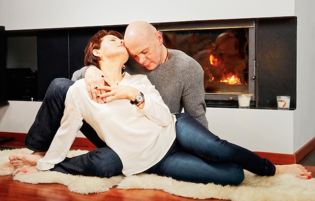 Romantyczna para brunetka i łysy mężczyzna siedzący z pasją na futrzanym dywanie przy kominku. Płonie ogień w kominku.