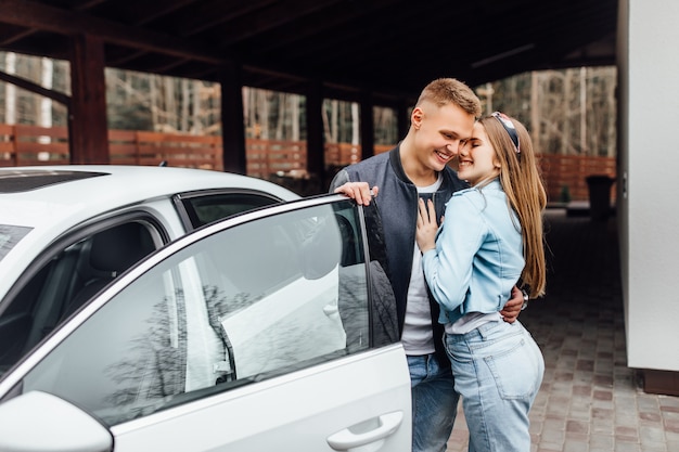Romantyczna para stoi w pobliżu nowego białego samochodu w domu i przytula.