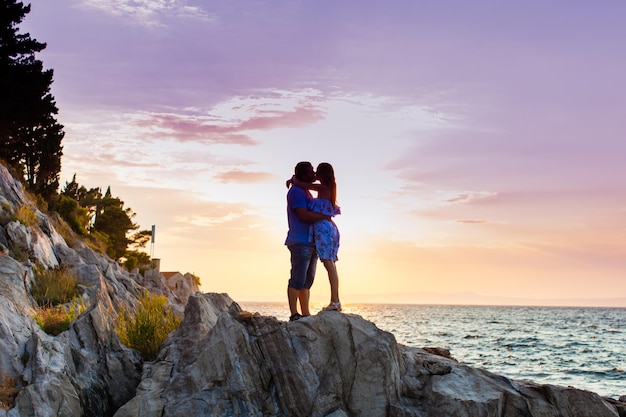 romantyczna para stojąca na skałach nad morzem na fioletowym dramatycznym tle zachodu słońca