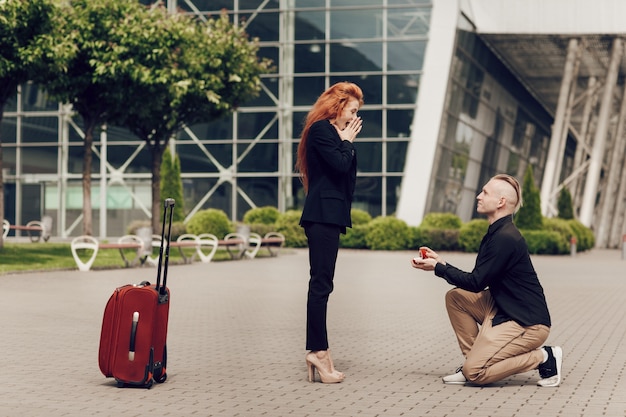Zdjęcie romantyczna para stojąca w pobliżu lotniska z walizką