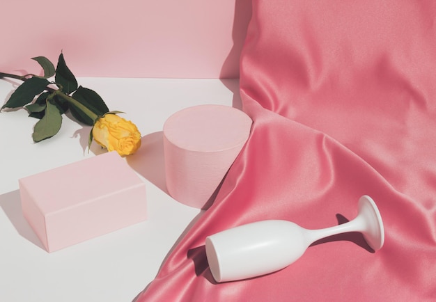 Romantyczna pastelowo różowa kompozycja z kieliszkiem do wina satynową zasłoną żółty kwiat róży i pustymi podium