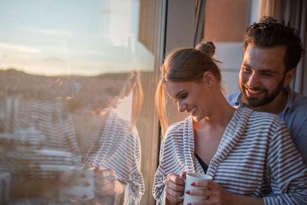 romantyczna szczęśliwa młoda para ciesząca się wieczorną kawą i pięknym zachodem słońca krajobraz miasta, stojąc przy oknie