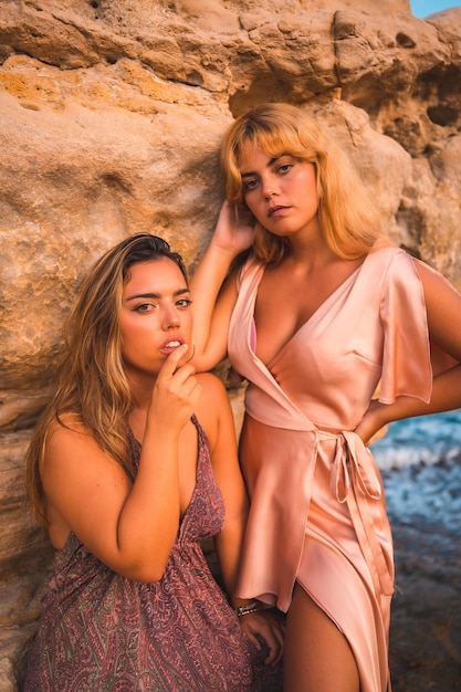 Romantyczne spojrzenia pary kaukaskich dziewcząt w różowych sukienkach, pozujących w letnim zachodzie słońca na plaży na skałach
