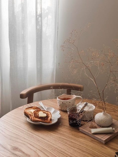 Romantyczne toasty śniadaniowe z masłem w kształcie serca, herbata z dżemem z żurawiny na okrągłym drewnianym stole w salonie