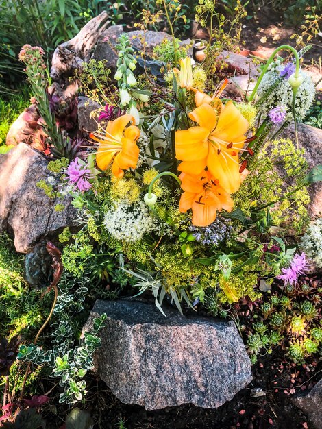 Romantyczny bukiet kwiatów farmowych otoczonych kamieniami Kompozycja zawiera kwiaty lilii monarda allium naparstnicy kwiatostany pietruszki pasternak czosnek strzały i liście piołunu