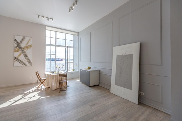 Romantyczny stół jest serwowany dla dwóch przy ogromnym oknie w mieszkaniu o otwartym planie w nowoczesnym stylu z jasnymi ścianami i drewnianymi podłogami