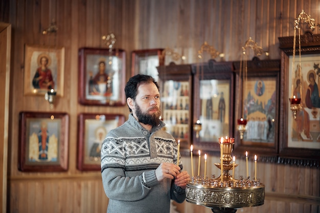 Zdjęcie rosjanin z brodą stoi w kościele prawosławnym, zapala świecę i modli się przed ikoną.