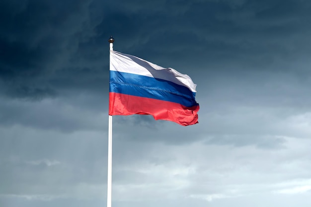 Rosyjska flaga na maszcie machającym na tle ciemnych, ponurych deszczowych chmur na niebie