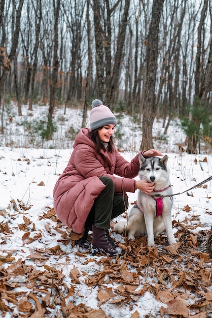 Rosyjska młoda dziewczyna przywiązała się do syberyjskiego husky z miłością na zimowym tle w lesie