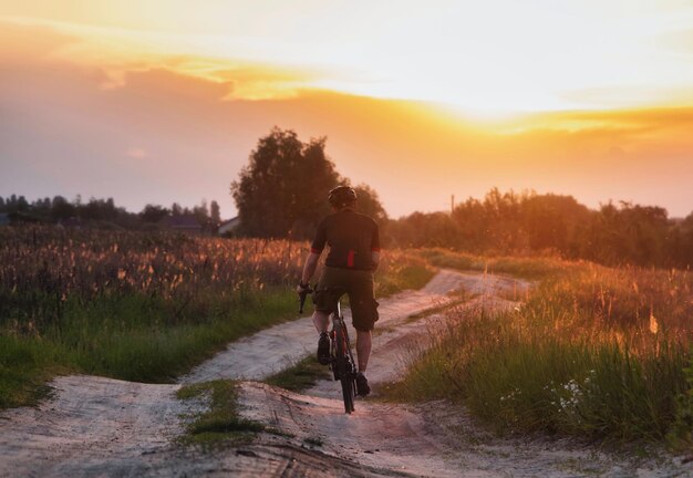 Rowerzysta jeżdżący ścieżką na polu na rowerze żwirowym na dramatycznym tle zachodu słońca Koncepcja sportu i aktywnego stylu życia