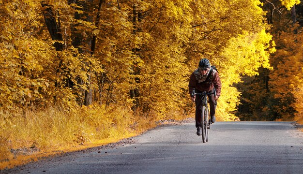 Rowerzysta jeździ drogą na rowerze w jesiennym lesie z żółtymi liśćmi.
