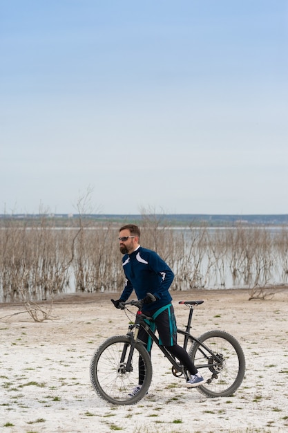 Rowerzysta na rowerze górskim na słonej plaży na tle trzcin i jeziora