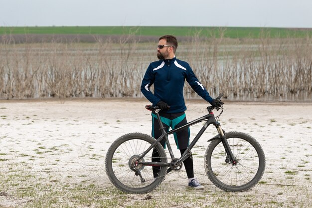 Rowerzysta na rowerze górskim na słonej plaży na tle trzcin i jeziora