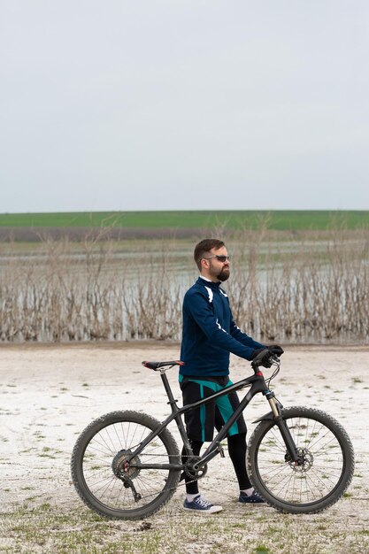 Rowerzysta na rowerze górskim na słonej plaży na tle trzcin i jeziora