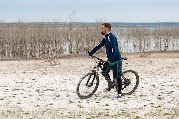 Rowerzysta na rowerze górskim na słonej plaży na tle trzcin i jeziora